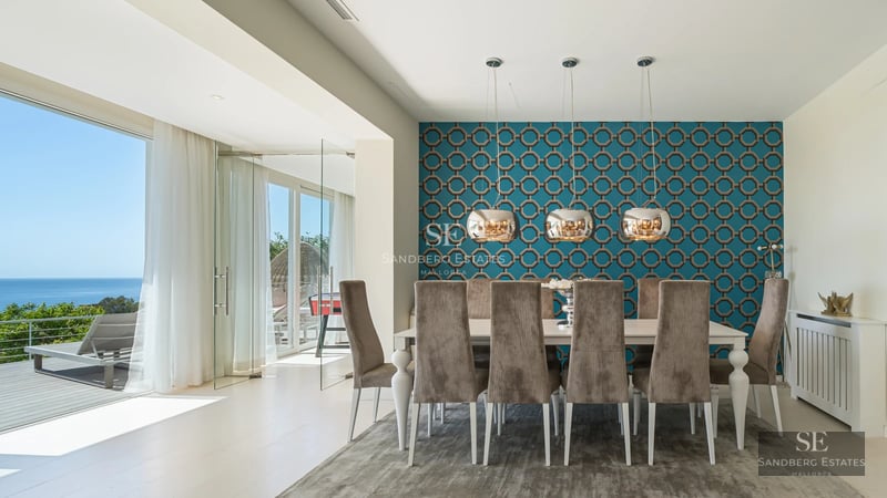 Wide view of bright living room with balcony and sea view. Modern furniture in neutral tones. Light wood flooring.