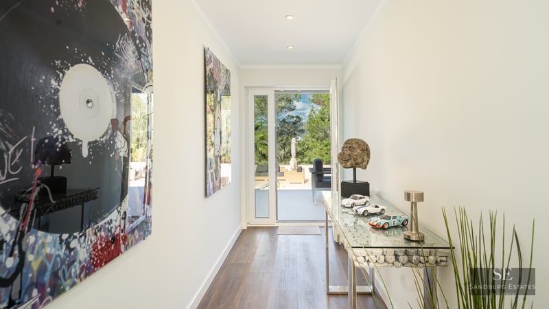 Couloir moderne lumineux avec du pop art vibrant, une console en verre et une porte ouverte sur une terrasse arborée.