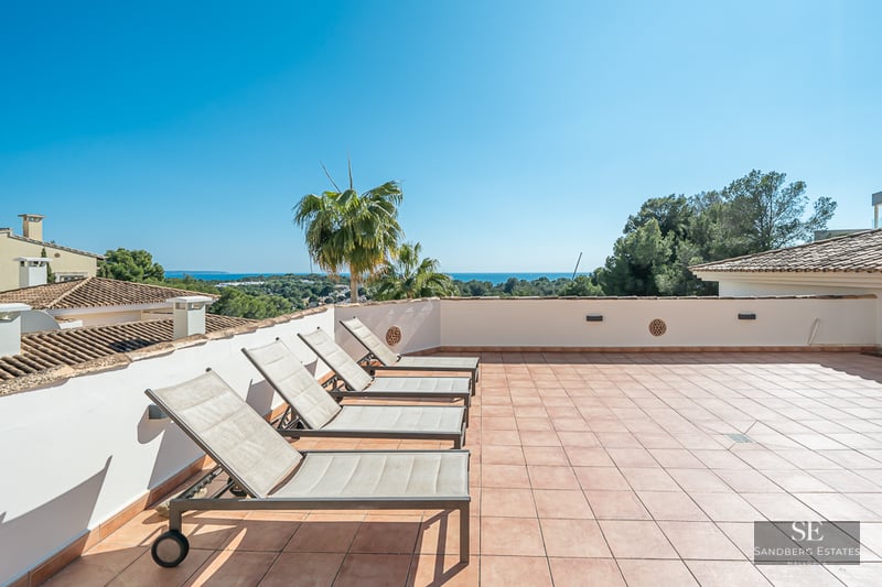 Grande terrasse en terre cuite avec quatre chaises longues et vue panoramique sur la mer sous un ciel bleu.