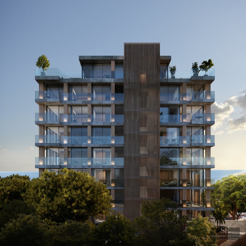 Modern multi-story building with glass balconies and wood accents surrounded by trees and sea views.