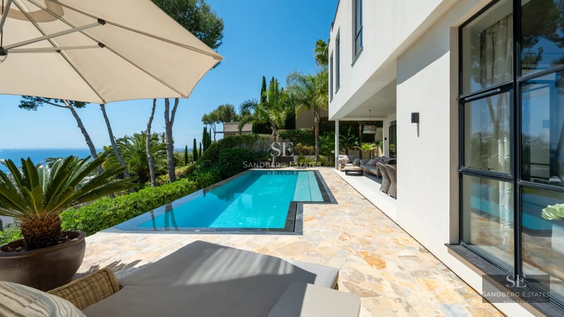 Exterior of a modern villa with an infinity pool. Minimalist architecture, manicured garden and unobstructed views. Stone and wood details.