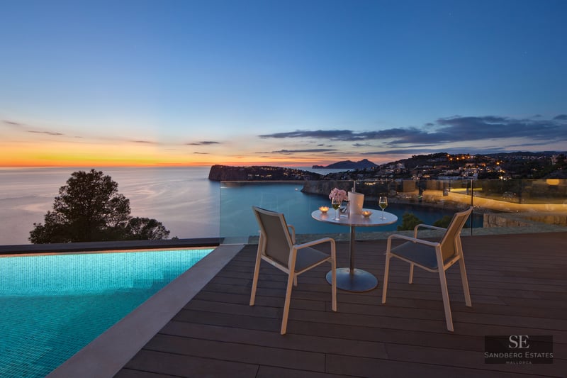 Luxury terrace with infinity pool, table for two, and panoramic sea view at sunset.