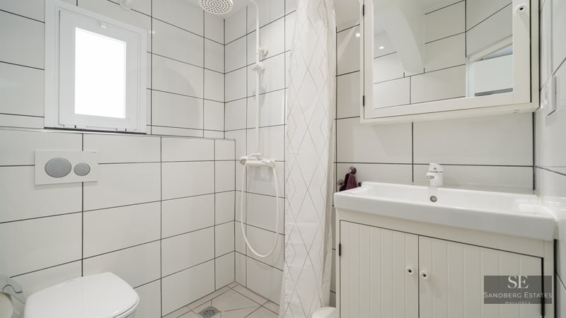 White tiled bathroom with a sink, toilet, and shower area separated by a white curtain.