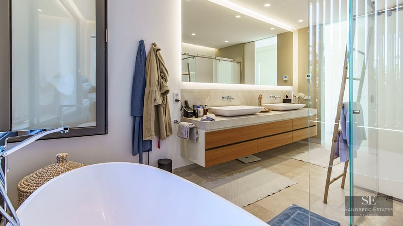 Salle de bain de luxe avec double vasque en bois, miroir rétroéclairé, douche en verre et baignoire îlot blanche.