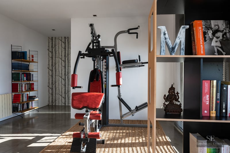 Home gym featuring a red weight machine, bookshelves, and polished concrete flooring.