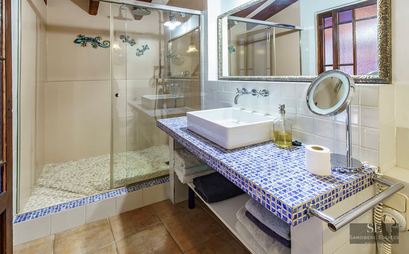 Modern bathroom featuring a walk-in shower with pebble floor and a blue mosaic tile vanity with a white vessel sink.