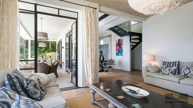Modern living room with grey sofas, a large white feather lamp, and glass doors opening to a lush terrace.