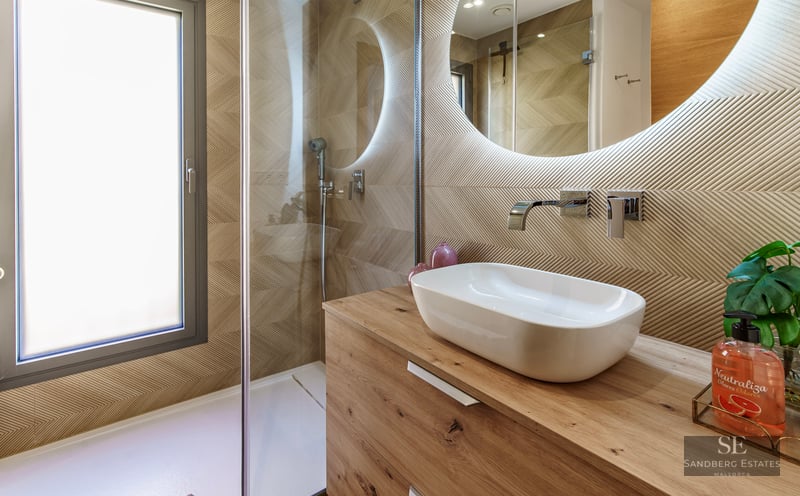 Modern bathroom featuring a wooden vanity, vessel sink, backlit round mirror, and a walk-in shower with glass screen.