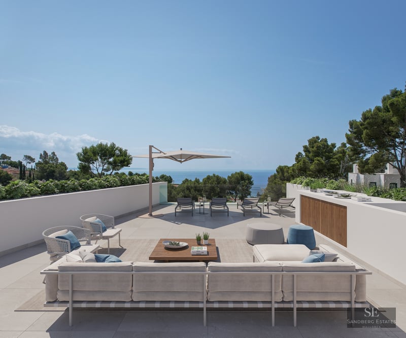 Large modern terrace with sofas, sunbeds, and an expansive view of the sea under a clear blue sky.