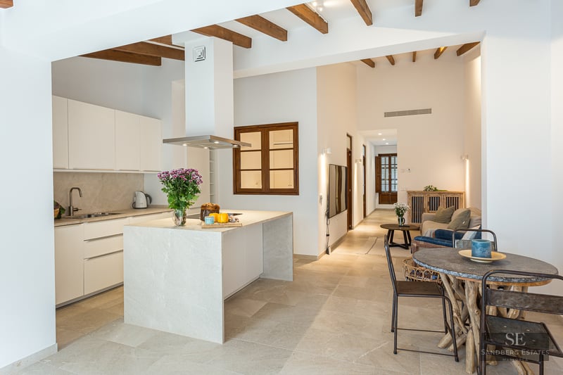 Bright open-plan kitchen featuring a stone island, wooden ceiling beams, and a rustic dining area.