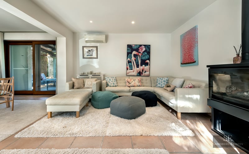 Modern living room featuring a white leather sectional sofa, colorful poufs, a plush rug, and a wood-burning fireplace.