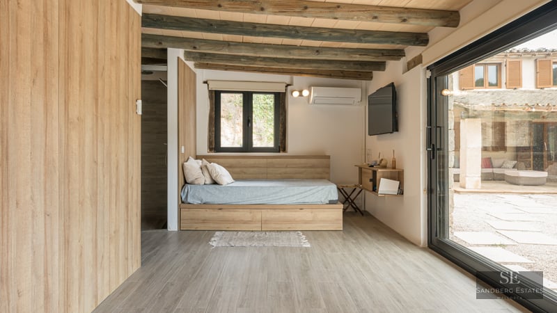 Modern bedroom featuring a wooden platform bed, rustic ceiling beams, and a large sliding door leading to a patio.