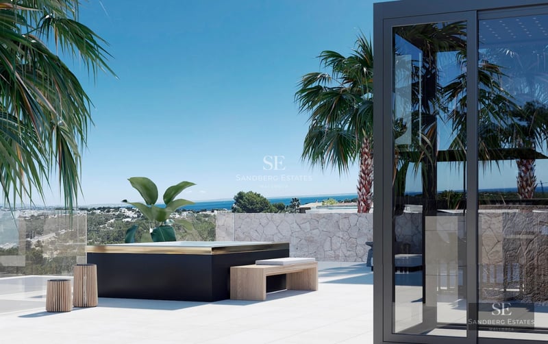 Spacious balcony with sea view. Modern furniture, glass railing, and light-colored tiling. Visible vegetation.
