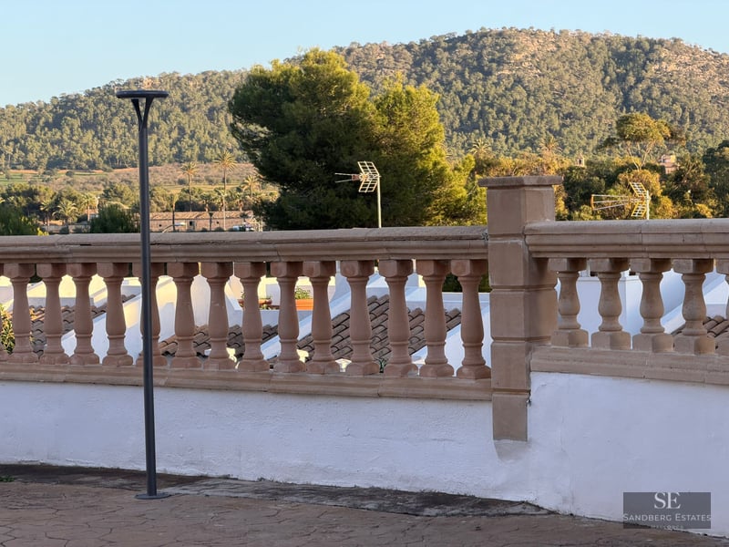 A stone balustrade on a white terrace overlooking a lush green mountain under a clear sky.