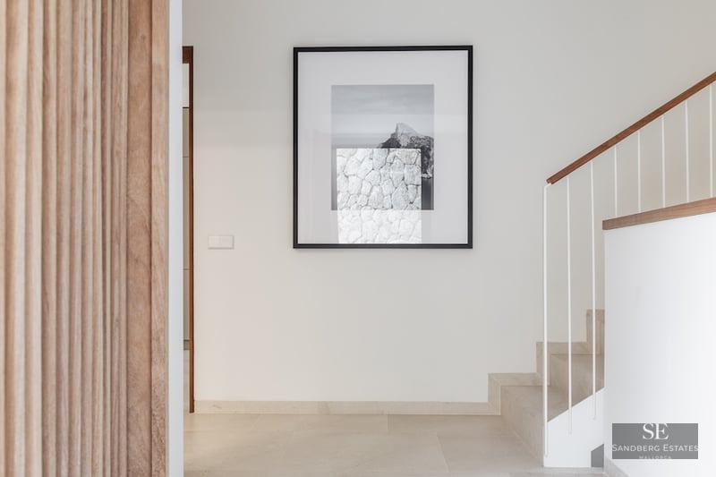 Bright hallway featuring a stone staircase with white railings, a wooden slatted wall, and a large framed artwork.