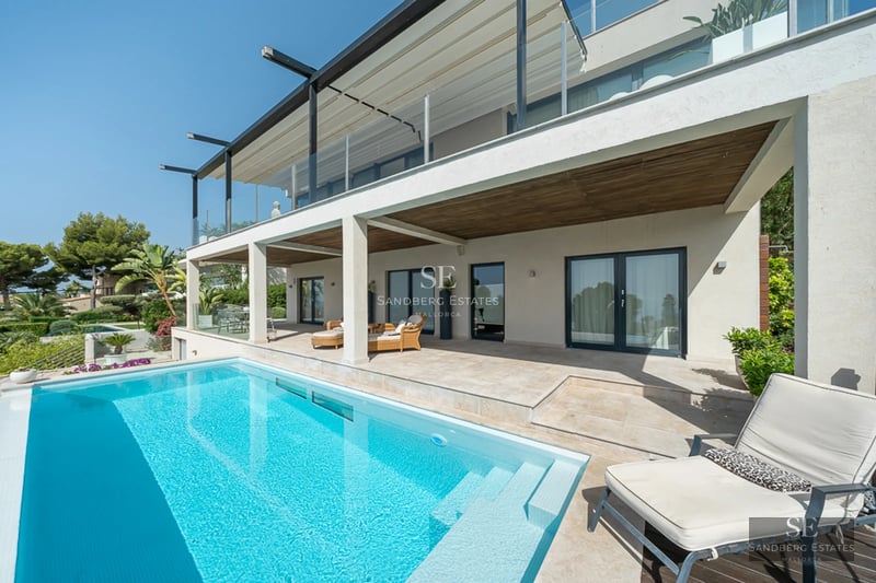 Spacious balcony with sea view. Wooden floors, glass railing, modern outdoor furniture, and a neutral color palette.