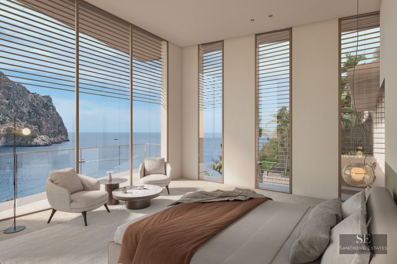 Modern bedroom with floor-to-ceiling windows overlooking the ocean and cliffs, beige armchairs, and minimalist decor.