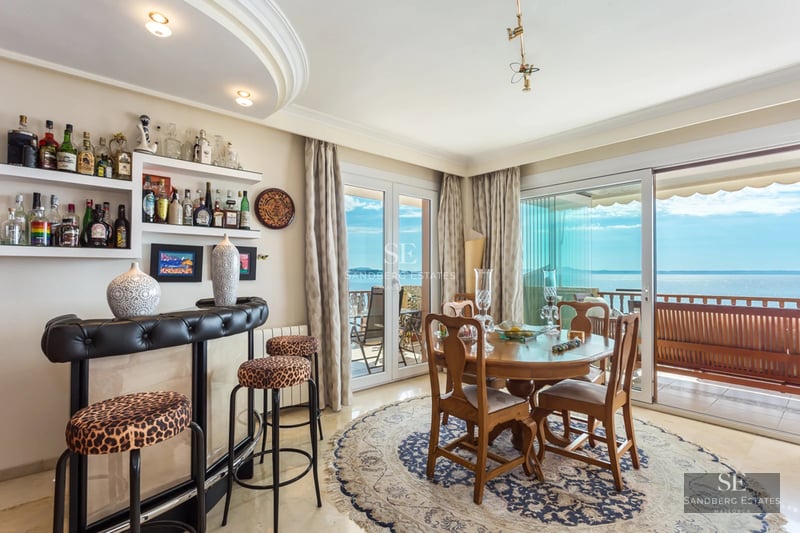 Dining area with a wooden table, leopard print stools, a home bar, and glass doors leading to a balcony with sea views.