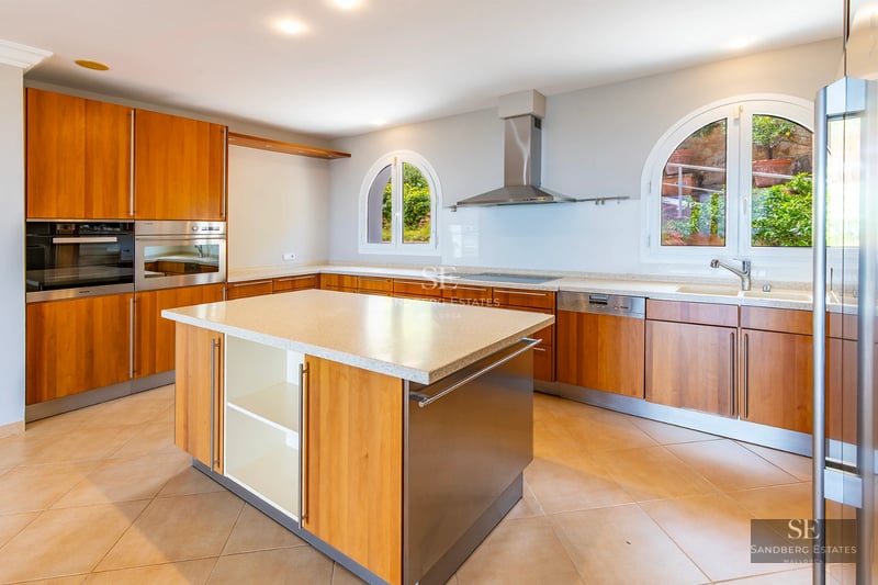 Expansive pool surrounded by lush greenery, with a modern villa in the background and a bright blue sky. Luxury and serenity.