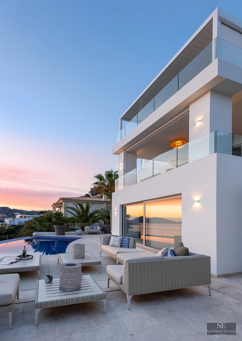 Spacious living room with large windows, light wood floors, modern furniture, and access to a terrace with a pool. Bright, elegant design.