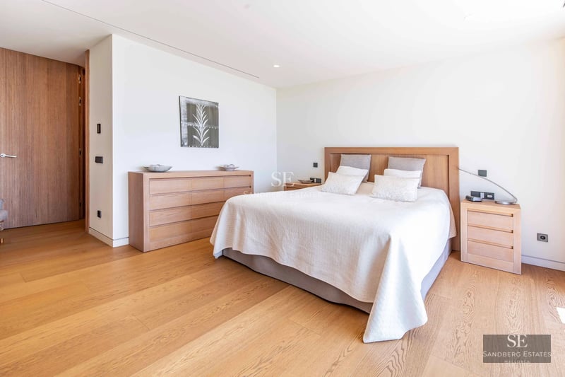 Spacious living room with picture windows, light wood floors, minimalist decor, and panoramic sea views. Beige sofa and modern rug.