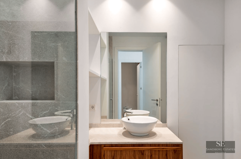 White ceramic vessel sink on a wood vanity, large mirror, and grey veined stone shower wall.