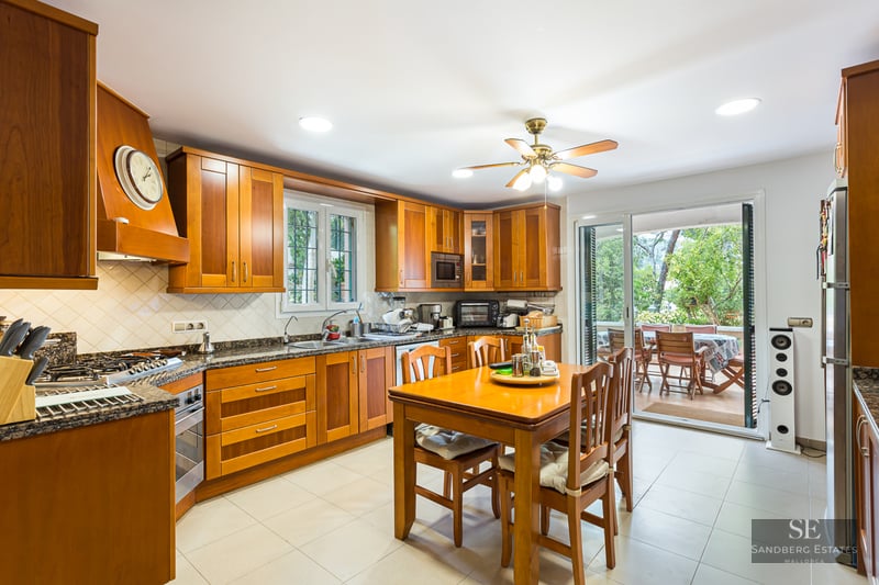 Traditional wooden kitchen with granite counters, dining table, and glass doors leading to a terrace.