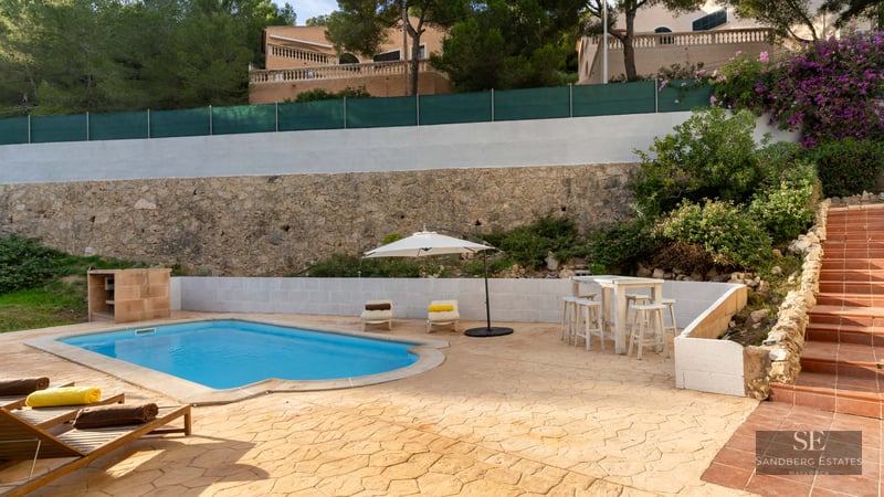 Piscine privée avec chaises longues, parasol blanc et mur en pierre rustique en arrière-plan.