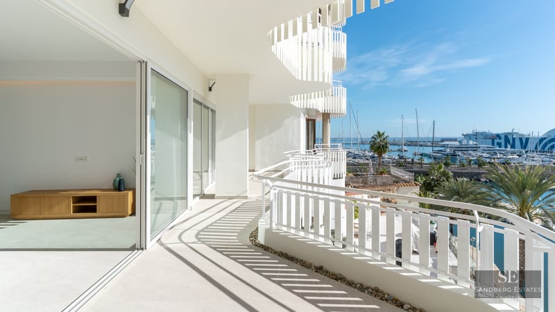 Spacious white curved balcony overlooking a sunny marina filled with boats and palm trees under a clear blue sky.