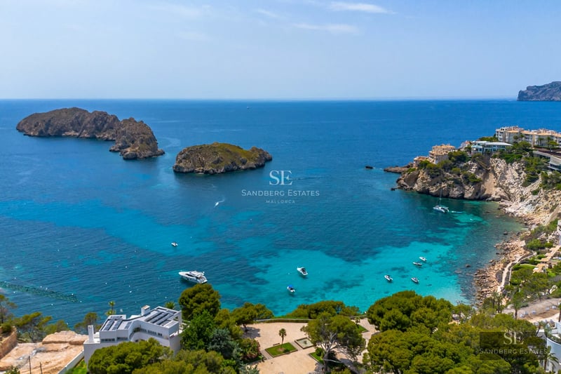 View of a luxurious infinity pool with stone edging, modern sun loungers, and lush greenery. Minimalist architecture, blue sky.