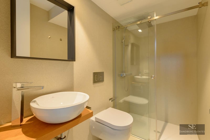 Contemporary bathroom featuring a white vessel sink on wood, wall-hung toilet, and a glass-enclosed walk-in shower.