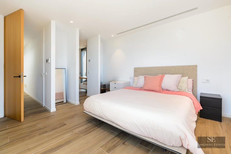 Bright, modern bedroom featuring a large bed with pink pillows, light wood floors, and white walls.