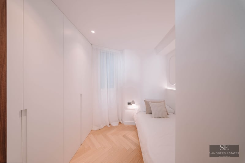 Bright bedroom featuring white built-in closets, herringbone wood floors, and a single bed with soft lighting.