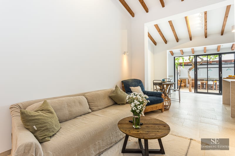 Living room with a beige sofa, wooden coffee table, exposed ceiling beams, and glass doors opening to a patio.