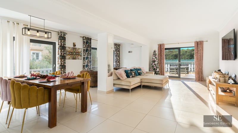 Espace de vie lumineux avec chaises en velours moutarde, canapé beige et grandes baies vitrées ouvrant sur une terrasse.