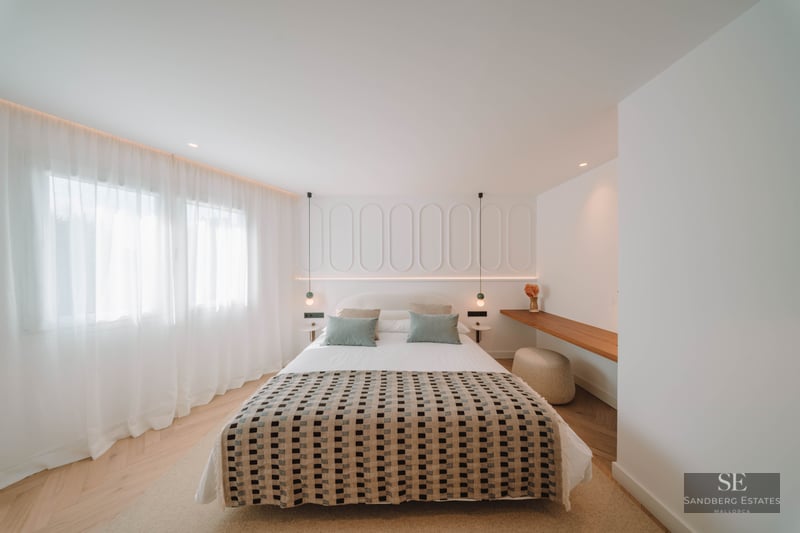 A bright, modern bedroom featuring a patterned bedspread, white paneled headboard wall, and herringbone wood flooring.