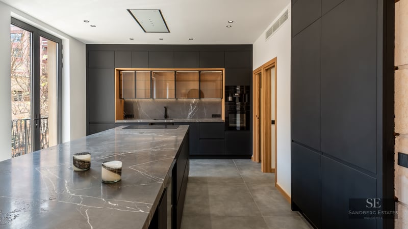 Modern kitchen featuring matte black cabinetry, grey veined marble countertops, and large windows.