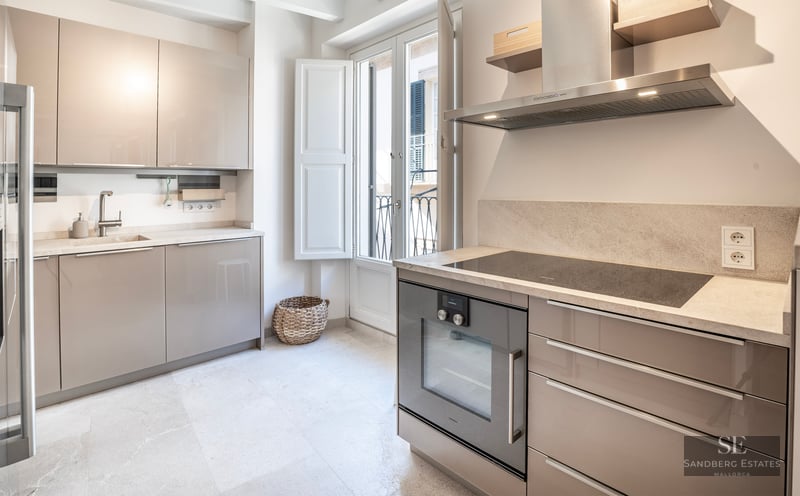 Cuisine moderne lumineuse avec placards beige brillant, plan de travail en pierre et porte-fenêtre.