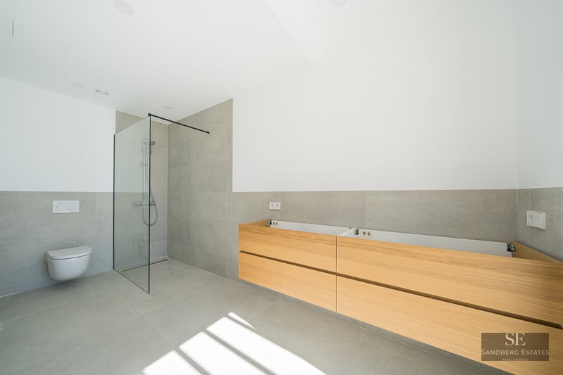 Modern bathroom with grey tiles, glass walk-in shower, wall-mounted toilet, and wooden vanity unit.
