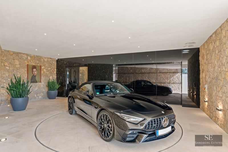 A black Mercedes sports car on a circular rotating platform in a modern garage with natural stone walls and mirrors.