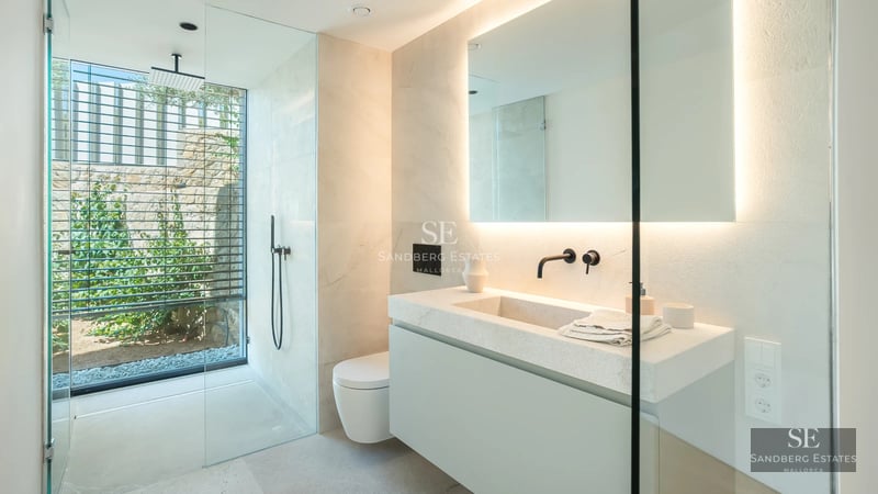 Large balcony overlooking the sea. Glass railing, wooden floor, modern outdoor furniture and infinity pool in the background.