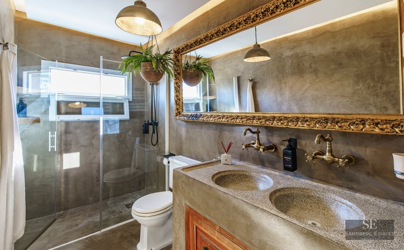 Luxury bathroom featuring microcement walls, an ornate gold mirror, double vanity, and glass shower enclosure.