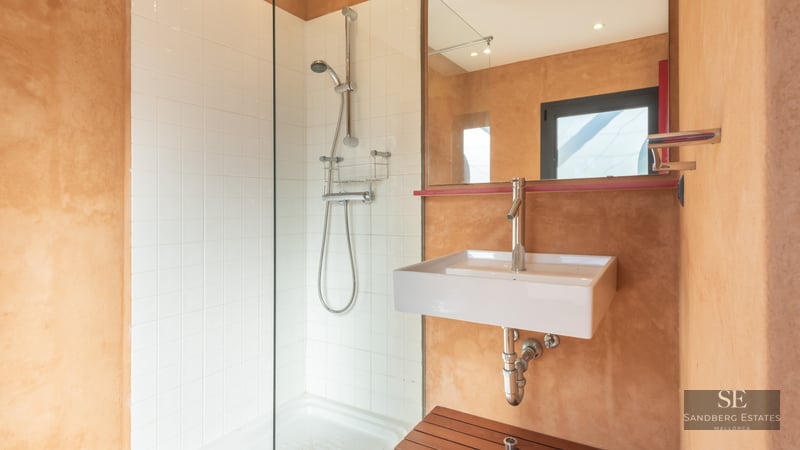 Modern bathroom featuring a walk-in glass shower, white square tiles, and warm terracotta textured walls with a white sink.