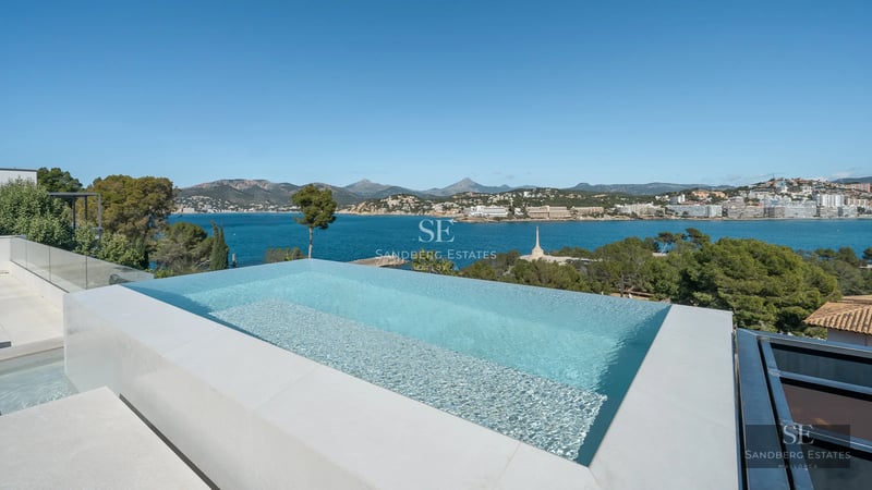 View of modern infinity pool with elegant sun loungers and lush vegetation. Minimalist architectural design.