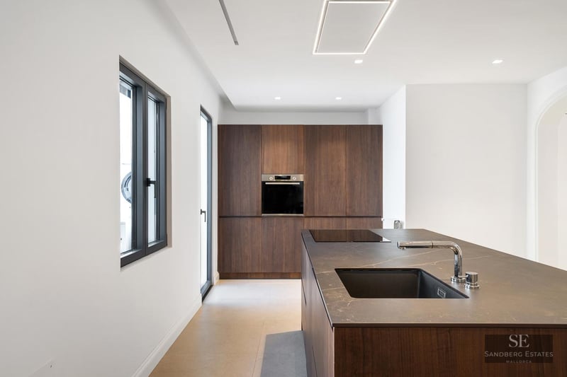 Modern kitchen featuring a dark wood island, black countertop, integrated sink, and full-wall built-in cabinetry.