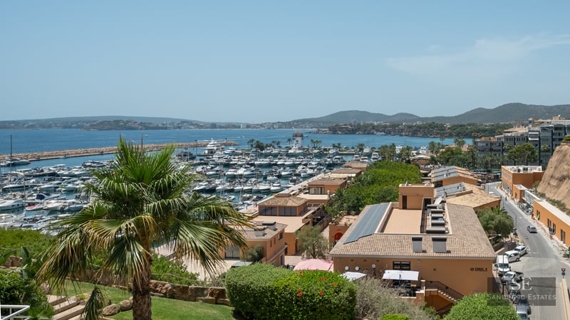 Elevated view of a Mediterranean marina filled with luxury yachts, overlooking the sea and coastline under a clear sky.