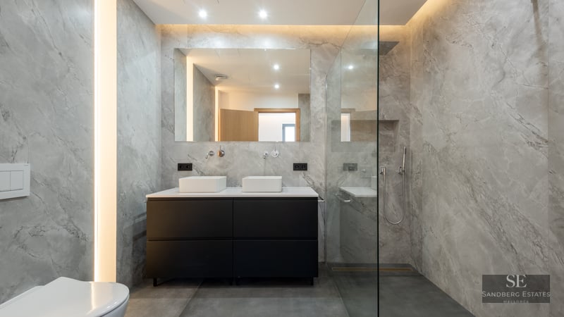 Elegant bathroom with gray marble walls, black double vanity, and glass walk-in shower.