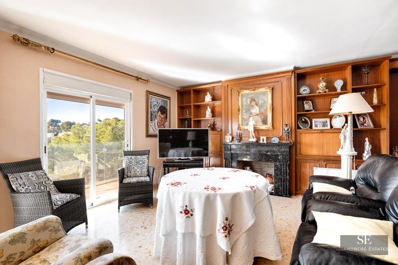 Living room with marble fireplace, wooden shelves, leather sofas, and glass doors looking out to trees.