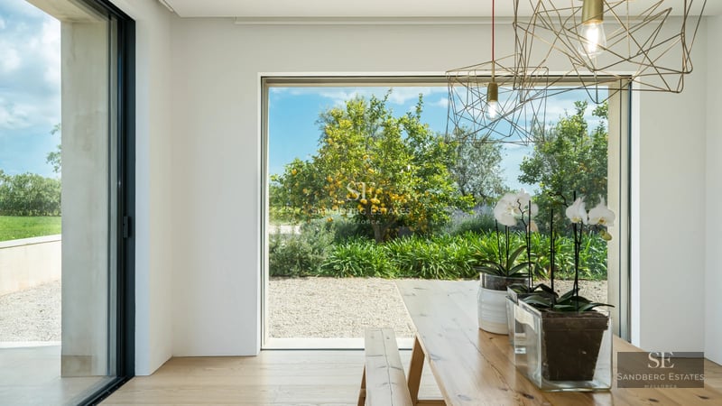 Modern living room with large windows, light wood flooring, grey sofas, and panoramic sea views. Abundant natural lighting.