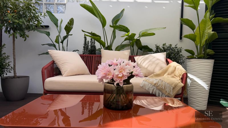 Red rope sofa with cream cushions on a terrace surrounded by tropical plants and a glossy orange coffee table.